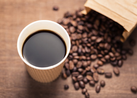 Paper cup filled with black coffee, with a spilled bag of coffee beans in the background