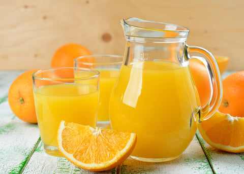 Pitcher and glasses of orange juice, decorated with whole and sliced fresh oranges